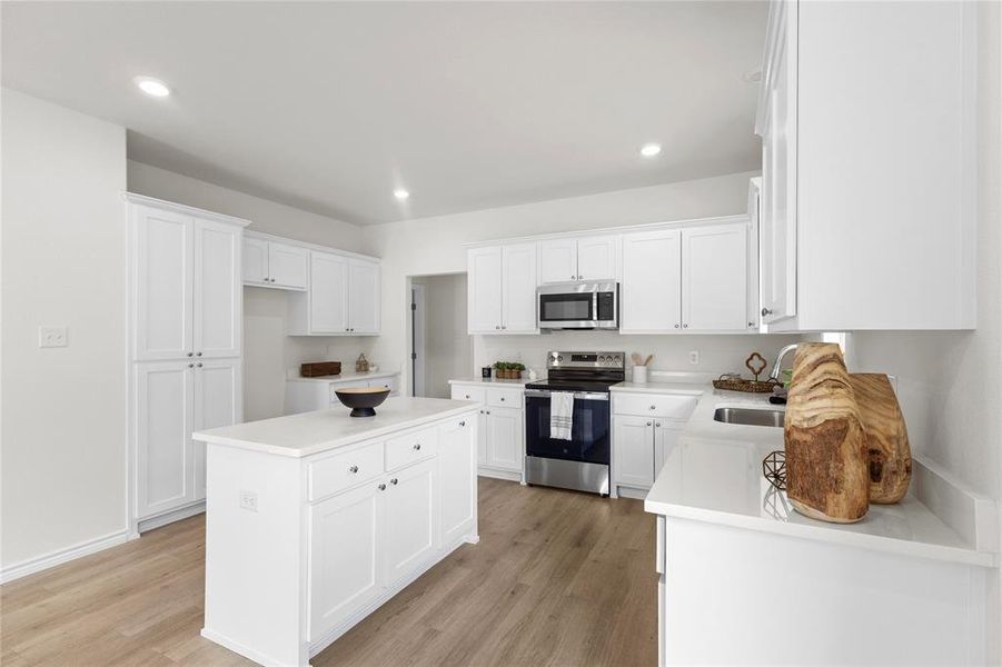 Kitchen with appliances with stainless steel finishes, white cabinets, a kitchen island, light wood-style flooring, and recessed lighting Kitchen with appliances with stainless steel finishes, white cabinets, a kitchen island, light wood-style flooring, and recessed lighting