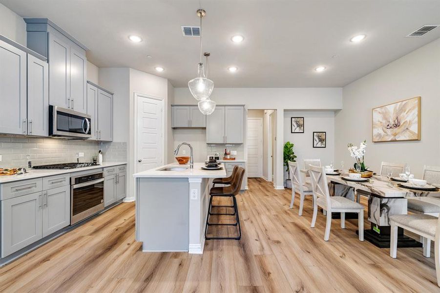 Kitchen with an island with sink, stainless steel appliances, light wood-type flooring, decorative light fixtures, and sink