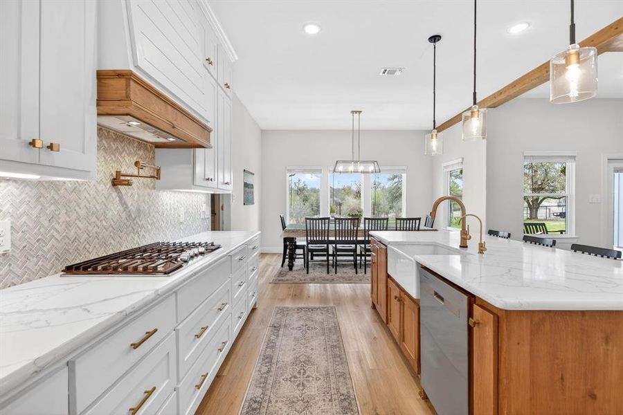 Kitchen with two tone color scheme, light stone countertops, stainless steel appliances, light wood-style floors, and a center island with sink Kitchen with two tone color scheme, light stone countertops, stainless steel appliances, light wood-style floors, and a center island with sink