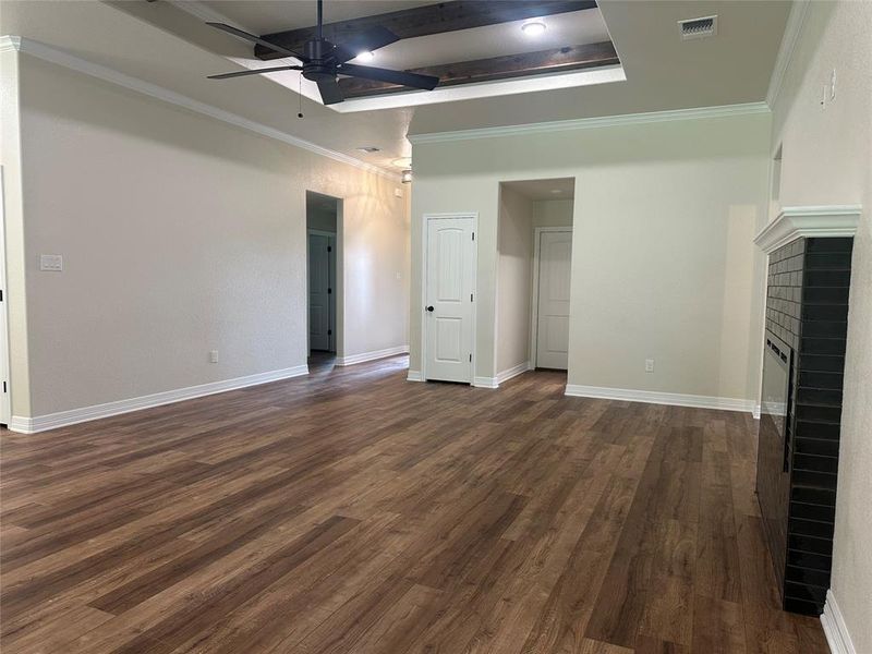 Unfurnished living room with ceiling fan, dark wood-type flooring, a raised ceiling, a fireplace, and crown molding Unfurnished living room with ceiling fan, dark wood-type flooring, a raised ceiling, a fireplace, and crown molding