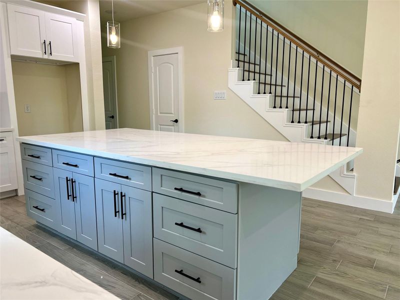 Modern kitchen with a spacious island featuring a sleek quartz countertop and ample cabinetry. The adjacent staircase has a stylish design with wooden handrails and black metal balusters, adding a touch of elegance to the open space. Modern kitchen with a spacious island featuring a sleek quartz countertop and ample cabinetry. The adjacent staircase has a stylish design with wooden handrails and black metal balusters, adding a touch of elegance to the open space.