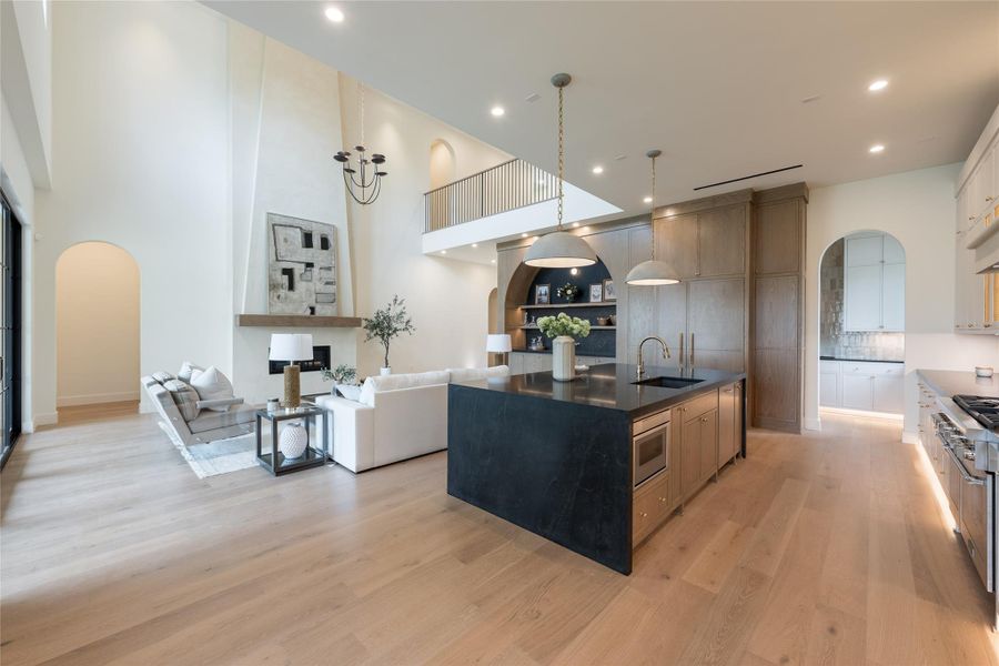 This view showcases the home’s central gathering space—where the sculpted black stone island and warm white oak cabinetry meet the drama of a double-height plaster fireplace wall, topped with a hand-scraped reclaimed oak mantel. Every finish, from the brass chain pendant lights to the softly curved arches and backlit cabinetry, reflects Elevare’s masterful balance of materiality and scale. This view showcases the home’s central gathering space—where the sculpted black stone island and warm white oak cabinetry meet the drama of a double-height plaster fireplace wall, topped with a hand-scraped reclaimed oak mantel. Every finish, from the brass chain pendant lights to the softly curved arches and backlit cabinetry, reflects Elevare’s masterful balance of materiality and scale.