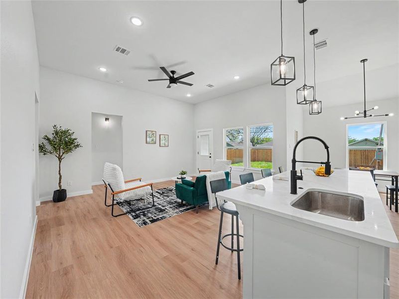 Kitchen featuring a breakfast bar, an island with sink, light stone countertops, light wood-style flooring, and open floor plan