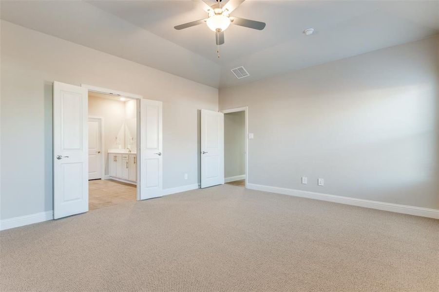 Unfurnished bedroom with light colored carpet, ceiling fan, ensuite bathroom, and lofted ceiling Unfurnished bedroom with light colored carpet, ceiling fan, ensuite bathroom, and lofted ceiling
