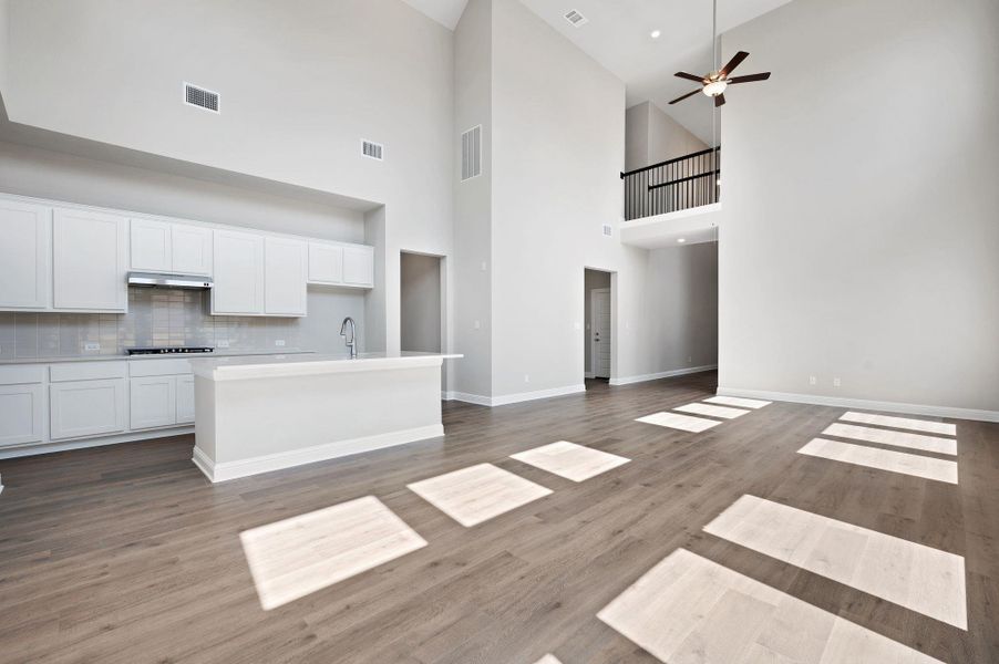 Kitchen featuring open floor plan, an island with sink, white cabinets, wood finished floors, and tasteful backsplash