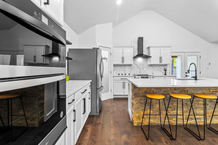 This modern kitchen features sleek white cabinetry, a central island with stone accents and stainless steel appliances, and a bright, open layout with high ceilings. Perfect for cooking and entertaining.