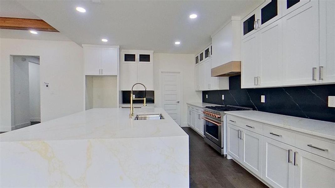 Kitchen with light stone countertops, stainless steel stove, recessed lighting, white cabinetry, and a kitchen island with sink