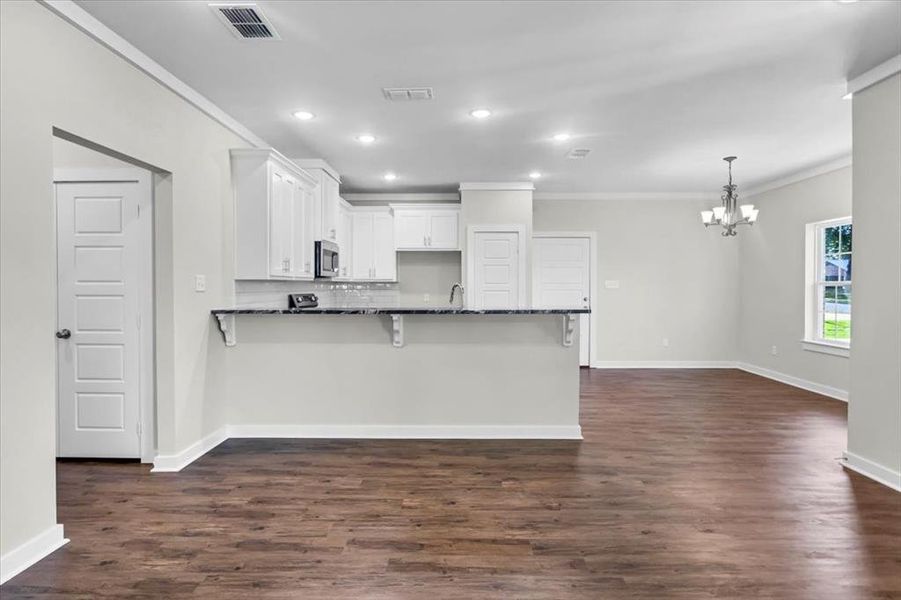 Kitchen with stainless steel microwave, a chandelier, ornamental molding, dark stone countertops, and white cabinets