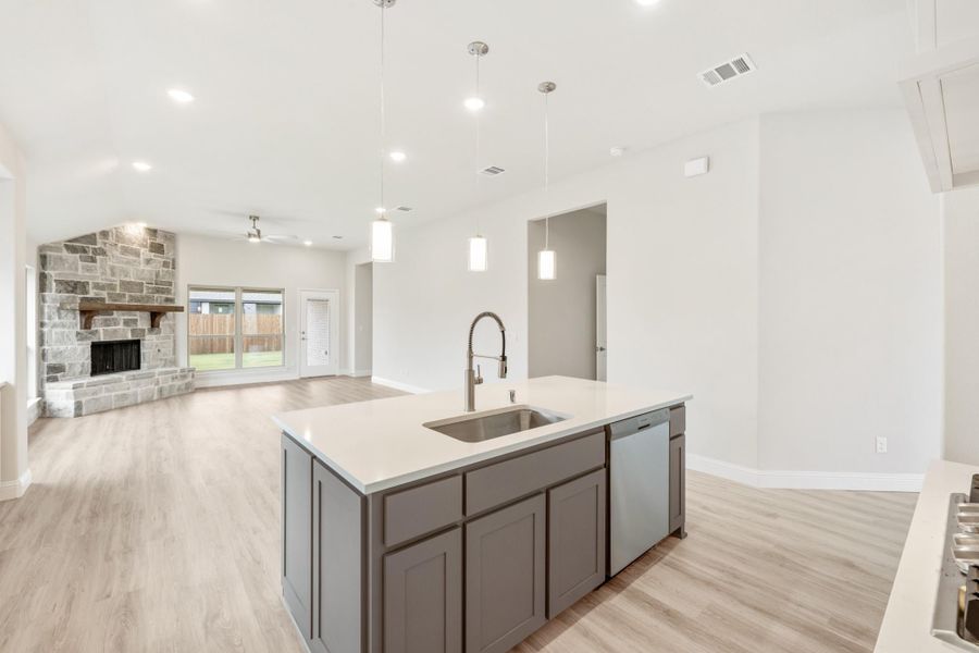 Kitchen island with gray cabinets and sink open to living room with stone fireplace and hardwood floors