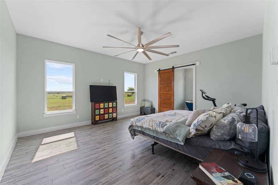 Spacious room featuring wood-finish flooring, two windows, and a large ceiling fan with integrated lighting