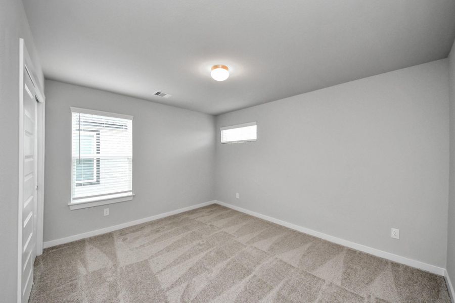 Secondary bedroom features plush carpeting, large windows that let in plenty of natural light, bright paint, and spacious closets. Sample photo of completed home with similar floor plan. Actual colors and selections may vary.