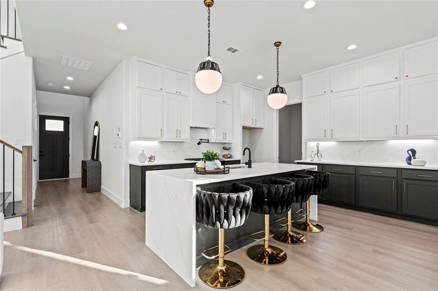 Kitchen featuring recessed lighting, light wood-type flooring, white cabinets, decorative backsplash, and a center island with sink