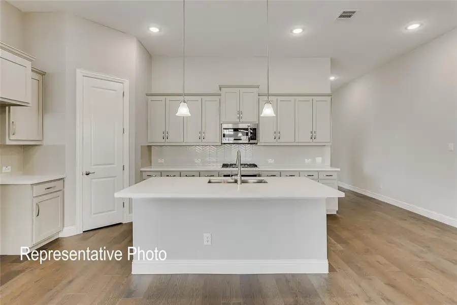Contemporary kitchen featuring a center island with an undermount sink and pendant lighting, light-toned cabinetry, stainless steel appliances including a built-in microwave, and wood-finish flooring