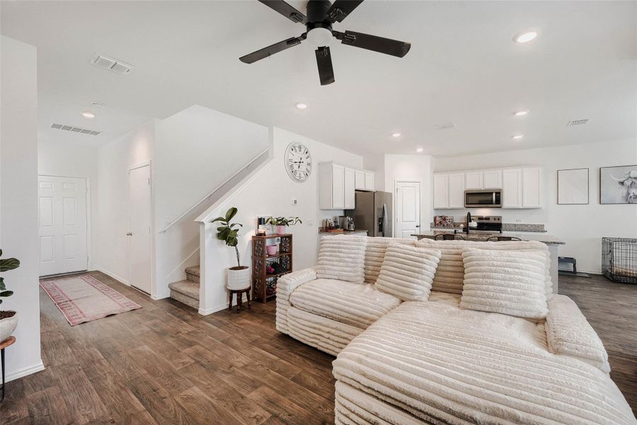 Open-concept living area with wood-finish flooring, a contemporary ceiling fan, recessed lighting, and a white painted staircase Open-concept living area with wood-finish flooring, a contemporary ceiling fan, recessed lighting, and a white painted staircase
