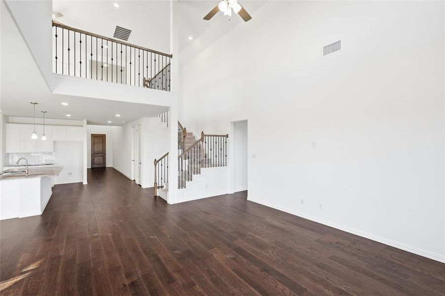 Two-story living area featuring dark wood-finish flooring, soaring ceilings, and a second-story overlook with decorative metal balusters