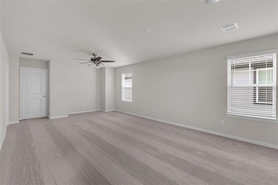 Primary bedroom with plenty of natural light coming in with a ceiling fan and neutral tone carpet.