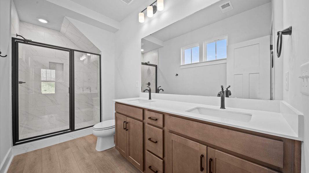 Accomplished design shines in this primary bath with dual vanity and a sleek tiled walk-in shower