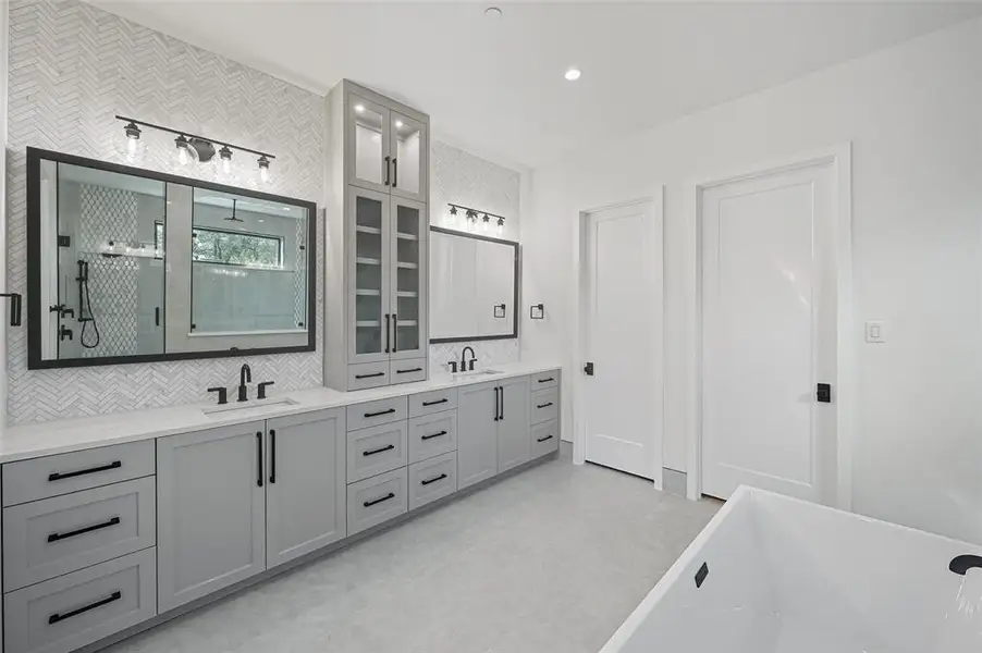 Example Spacious bathroom featuring an extended dual vanity with light gray cabinetry, matte black hardware, and an integrated tall linen cabinet with glass-front uppers Example Spacious bathroom featuring an extended dual vanity with light gray cabinetry, matte black hardware, and an integrated tall linen cabinet with glass-front uppers