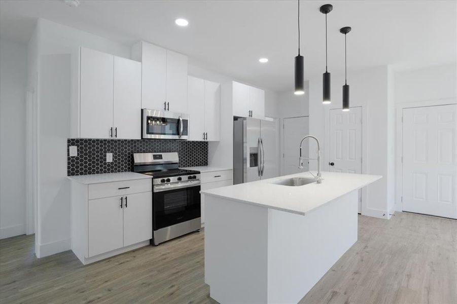 Kitchen featuring white cabinets, sink, stainless steel appliances, and hanging light fixtures