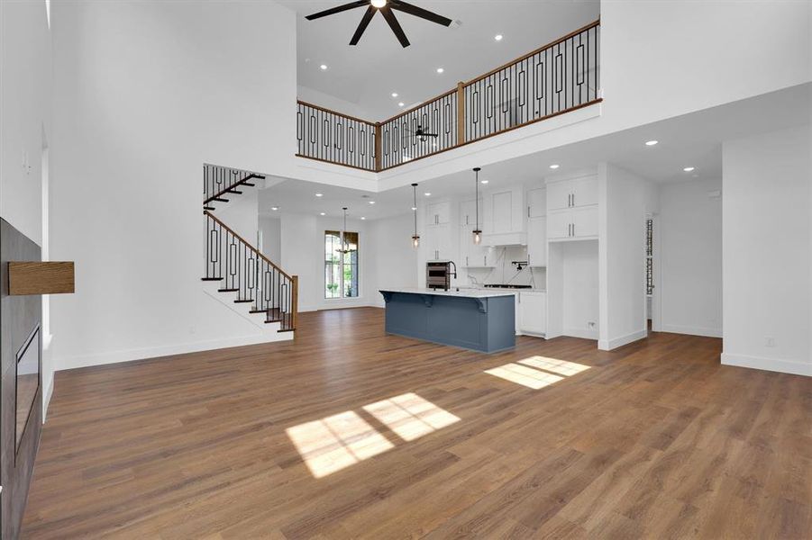 Unfurnished living room featuring a high ceiling, a ceiling fan, stairway, wood finished floors, and recessed lighting Unfurnished living room featuring a high ceiling, a ceiling fan, stairway, wood finished floors, and recessed lighting