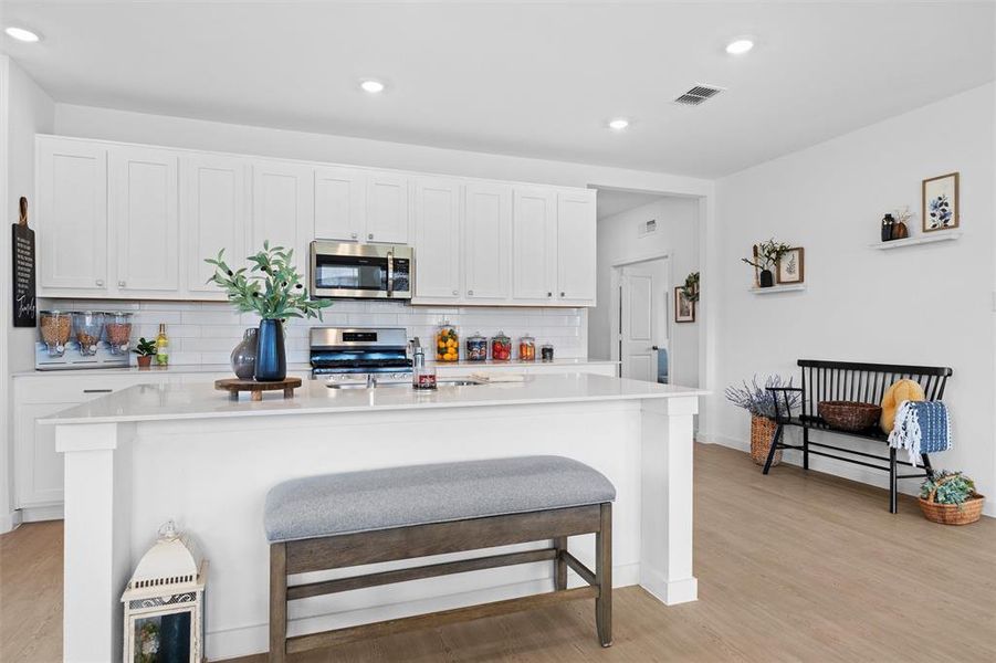 Kitchen with white cabinetry, stainless steel appliances, a breakfast bar, a center island with sink, and LVP type flooring Kitchen with white cabinetry, stainless steel appliances, a breakfast bar, a center island with sink, and LVP type flooring