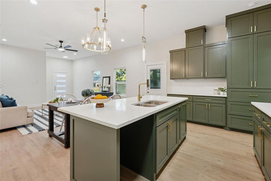 Kitchen with green cabinets, open floor plan, a center island with sink, hanging light fixtures, and light wood finished floors Kitchen with green cabinets, open floor plan, a center island with sink, hanging light fixtures, and light wood finished floors