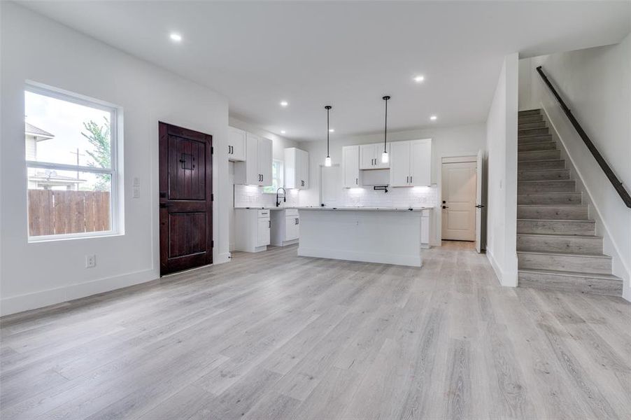 Unfurnished living room with plenty of natural light, stairway, light wood-type flooring, and recessed lighting Unfurnished living room with plenty of natural light, stairway, light wood-type flooring, and recessed lighting