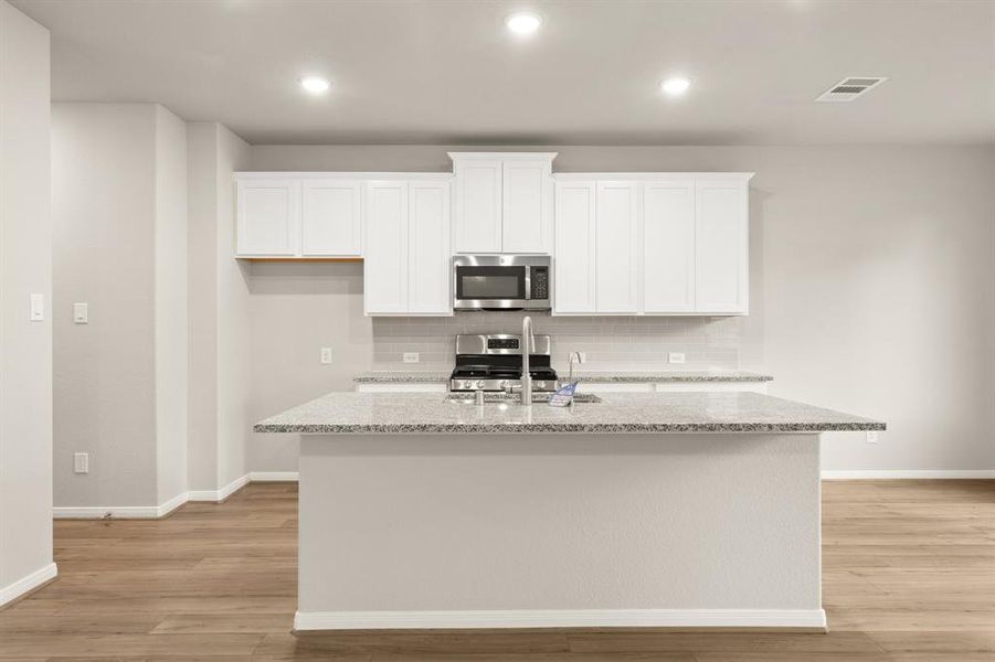 This light and bright kitchen features a large quartz island, white cabinets, a large sink overlooking your family room, recessed lighting, and beautiful backsplash.