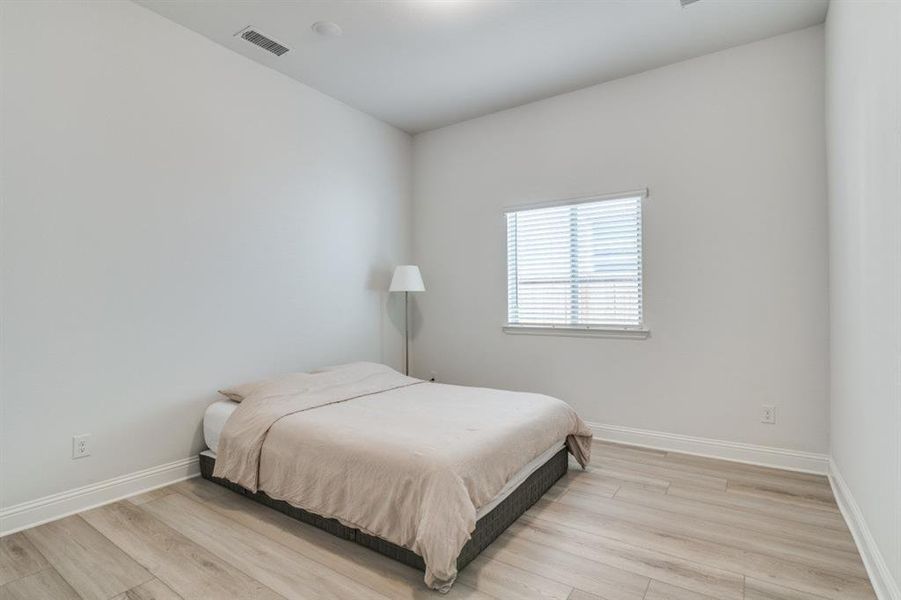 Bedroom featuring light wood finished floors, baseboards, and visible vents Bedroom featuring light wood finished floors, baseboards, and visible vents