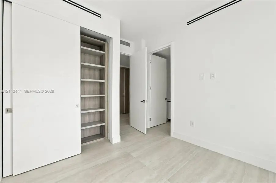 Minimalist interior featuring wood-finish flooring, recessed linear ceiling diffusers, sliding panel doors, and built-in shelving with wood-tone interior