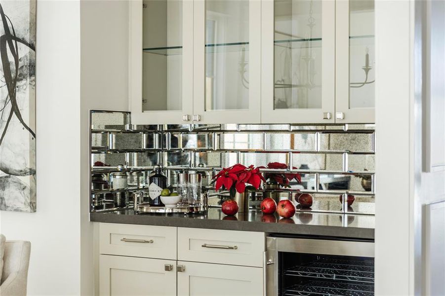 The bar area features mirrored tile backsplash for a touch of glamour, lower cabinets for storage, upper cabinets for displaying glassware and a wine refrigerator.