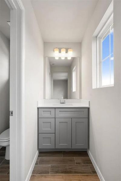 A window-lit bathroom with a stylish gray vanity and rich wood-look tile flooring.
