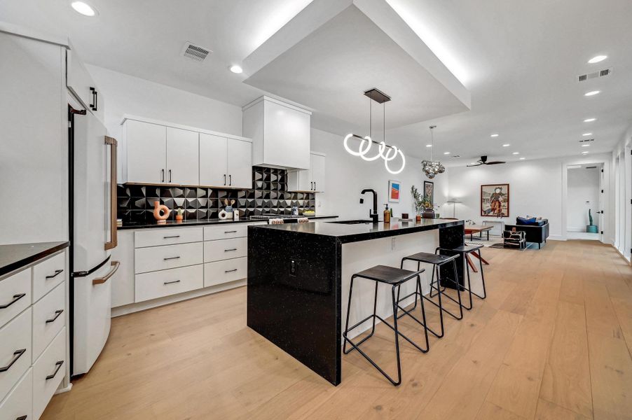 Kitchen with a breakfast bar, hanging light fixtures, a center island with sink, white cabinetry, and recessed lighting