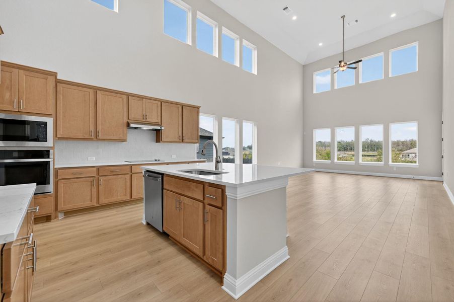 Kitchen with light wood-type flooring, appliances with stainless steel finishes, a center island with sink, and light stone countertops