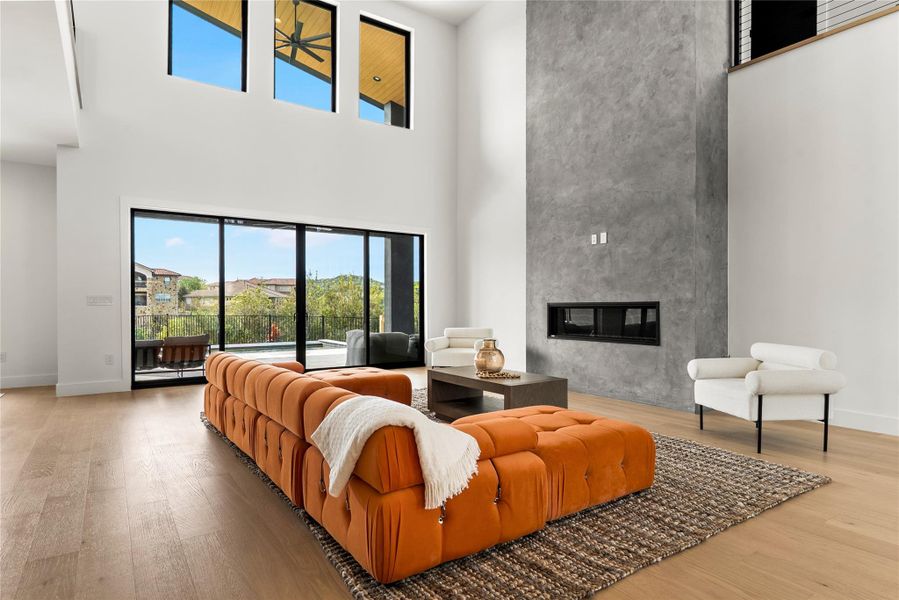 Living room with a high end fireplace, light wood finished floors, and a high ceiling Living room with a high end fireplace, light wood finished floors, and a high ceiling