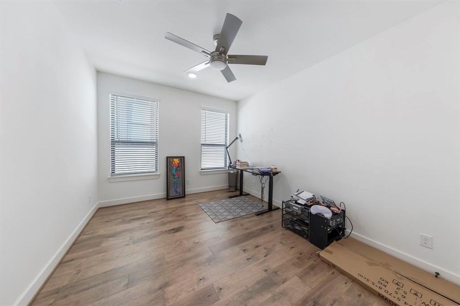 The secondary bedrooms showcase engineered wood flooring, a modern ceiling fan, and large windows that echo the home's cohesive design, offering a bright and inviting atmosphere.