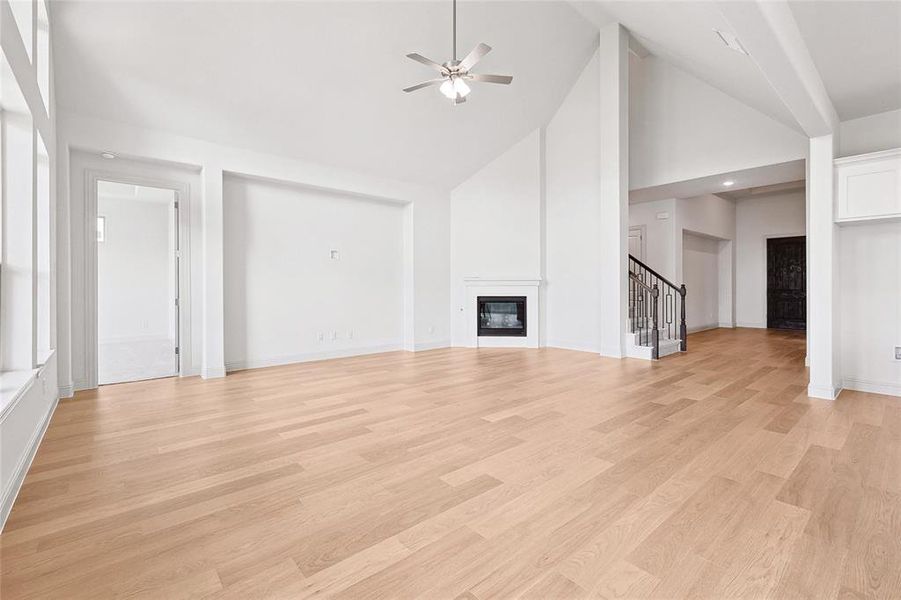 Unfurnished living room with high vaulted ceiling, ceiling fan, and light hardwood / wood-style flooring