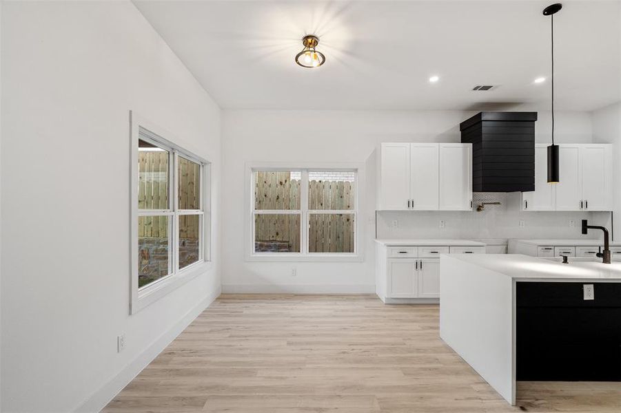 Kitchen with light hardwood / wood-style flooring, sink, decorative light fixtures, and white cabinets