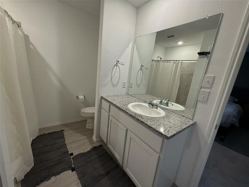 Bathroom featuring a white vanity with a speckled countertop, a large frameless mirror, and a built-in toilet Bathroom featuring a white vanity with a speckled countertop, a large frameless mirror, and a built-in toilet