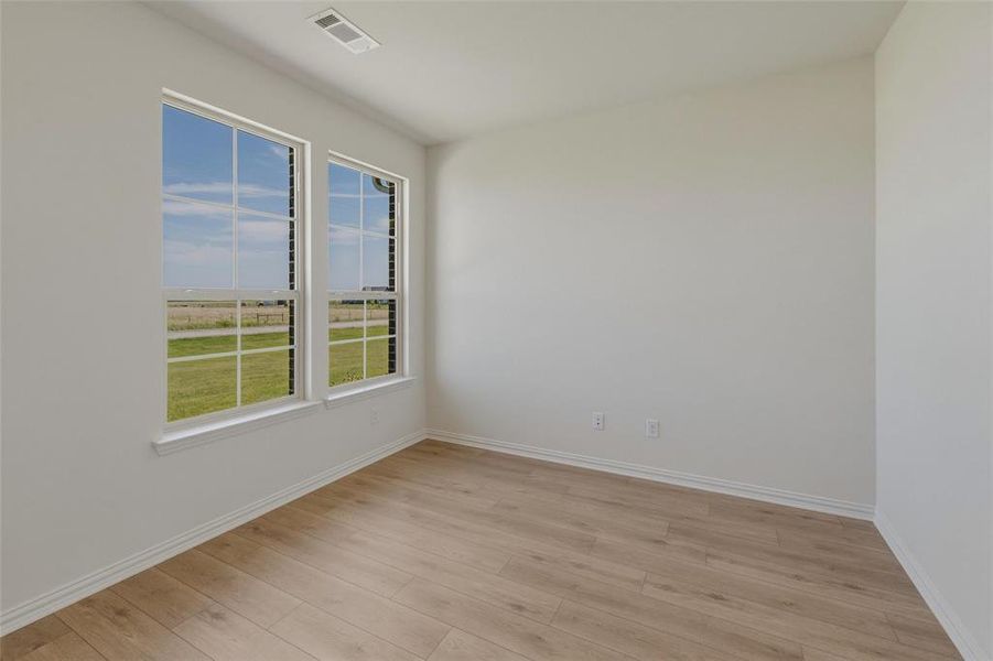 Light-filled interior space featuring two large windows, wood-finish flooring, white baseboards, and a neutral wall color Light-filled interior space featuring two large windows, wood-finish flooring, white baseboards, and a neutral wall color