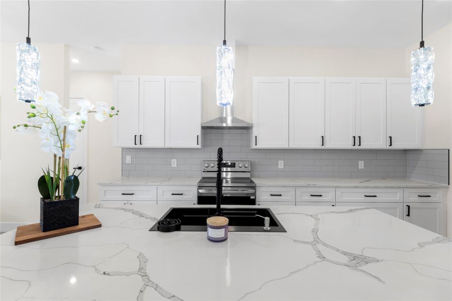 Kitchen featuring hanging light fixtures, light stone counters, white cabinetry, tasteful backsplash, and stainless steel electric range Kitchen featuring hanging light fixtures, light stone counters, white cabinetry, tasteful backsplash, and stainless steel electric range