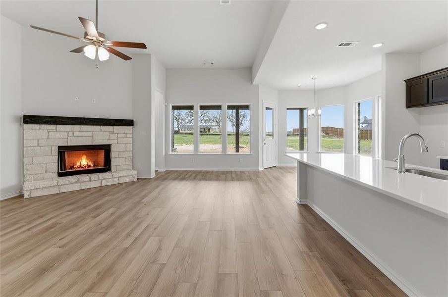 Unfurnished living room featuring a stone fireplace, light wood finished floors, ceiling fan, and hanging lights