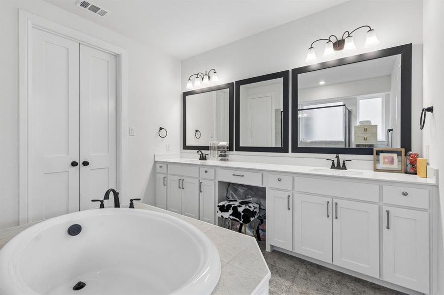 Bathroom featuring a large built-in soaking tub with black fixtures, an extended vanity with dual sinks, white shaker cabinetry, and individual framed mirrors
