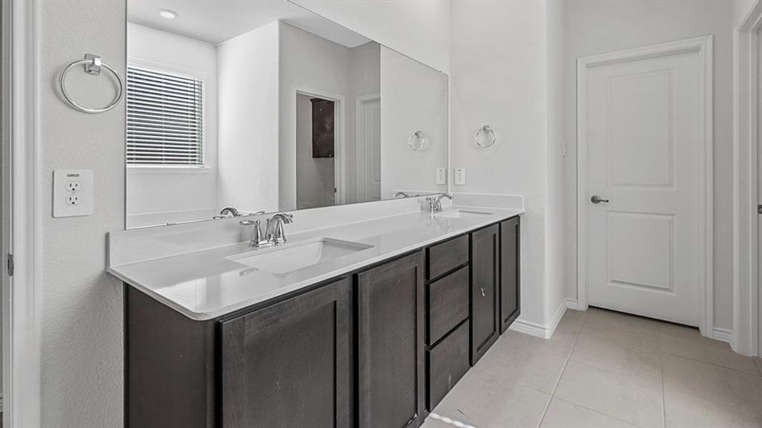 Dual vanity with dark wood-finish cabinetry, integrated sinks, chrome fixtures, and a large wall-mounted mirror