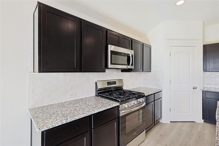 Kitchen with backsplash, stainless steel appliances, light hardwood / wood-style flooring, and light stone counters