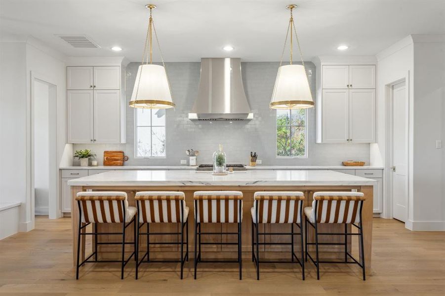 Kitchen with a healthy amount of sunlight, visible vents, an island with sink, and wall chimney exhaust hood Kitchen with a healthy amount of sunlight, visible vents, an island with sink, and wall chimney exhaust hood