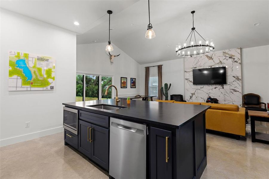 Kitchen featuring open floor plan, stainless steel appliances, a center island with sink, concrete floors, and vaulted ceiling