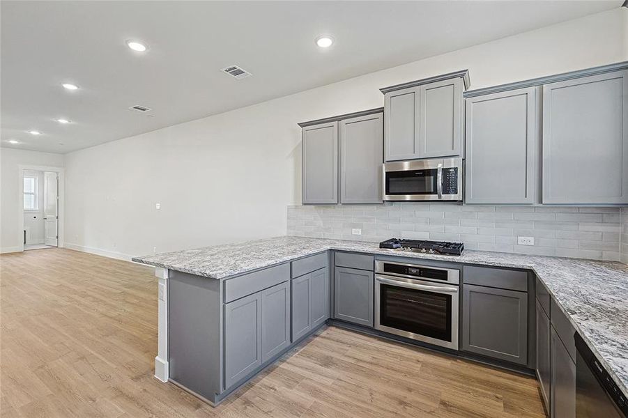 Kitchen featuring gray cabinets, decorative backsplash, recessed lighting, a peninsula, and stainless steel appliances