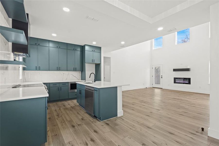 Kitchen with a glass covered fireplace, backsplash, an island with sink, recessed lighting, and light stone counters