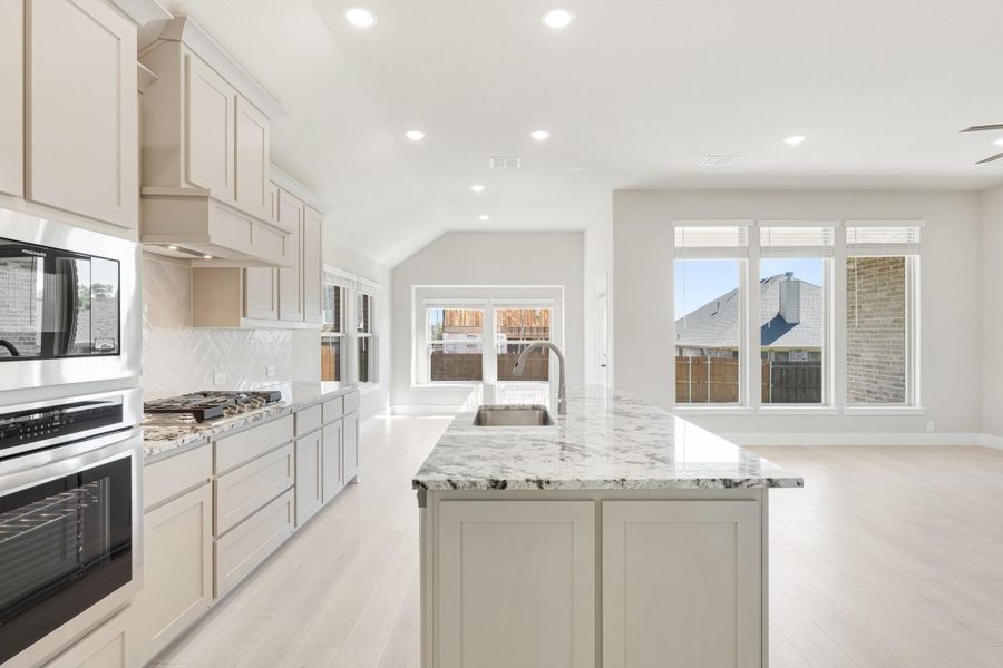 Open kitchen with granite island, cream cabinets, stainless appliances, and light wood floors